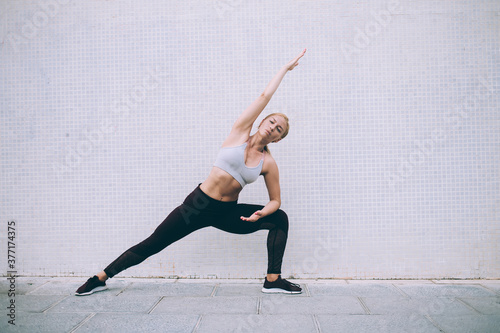 Portrait of young woman in stylish active wear doing yoga during morning workout at publicity area, sporty woman practicing healthy and energy lifestyle enjoying stretching training at urbanity