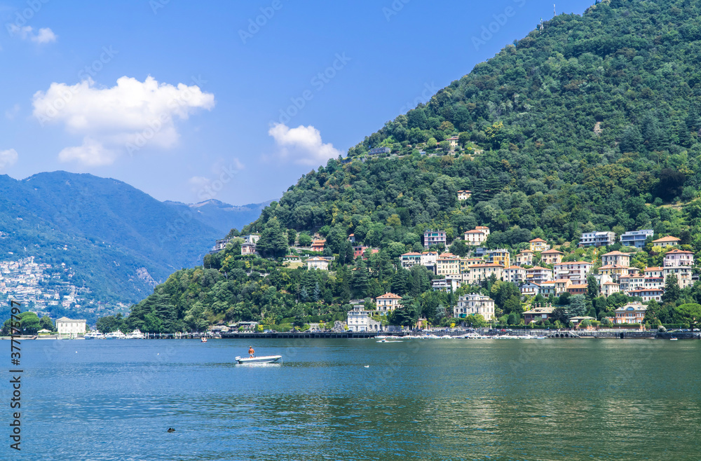 Man on small boat on Lake Como with towns and mountains in the background