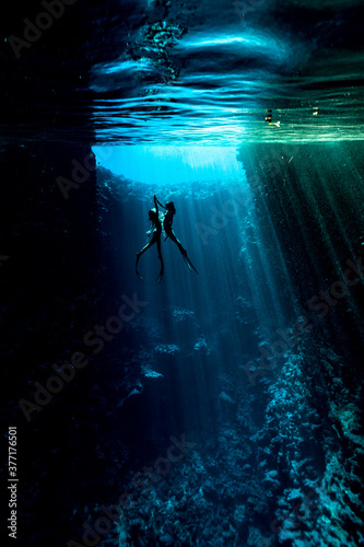 A female freedivers hand to hand diving in the cave with sun rays photo