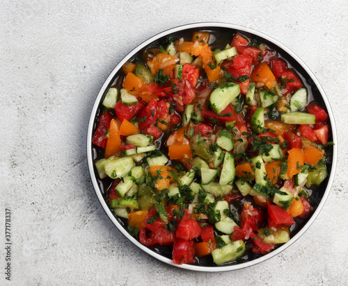 Cucumber, tomato and greens salad on a round plate on a light gray background. Top view, flat lay