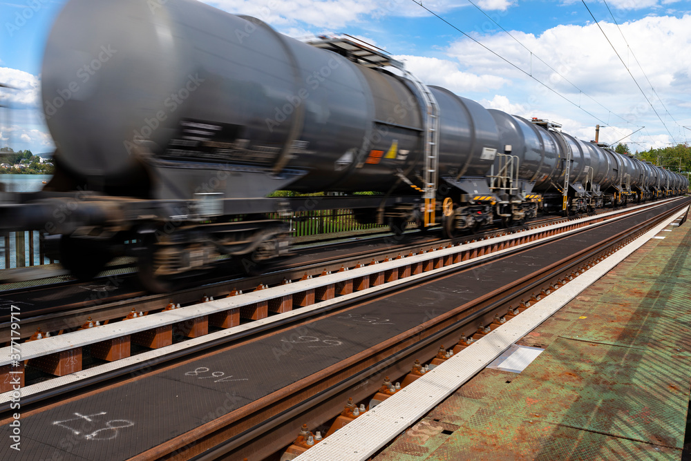 Naklejka premium Blurry photo of railroad tank cars in motion, on a metal bridge over the river.