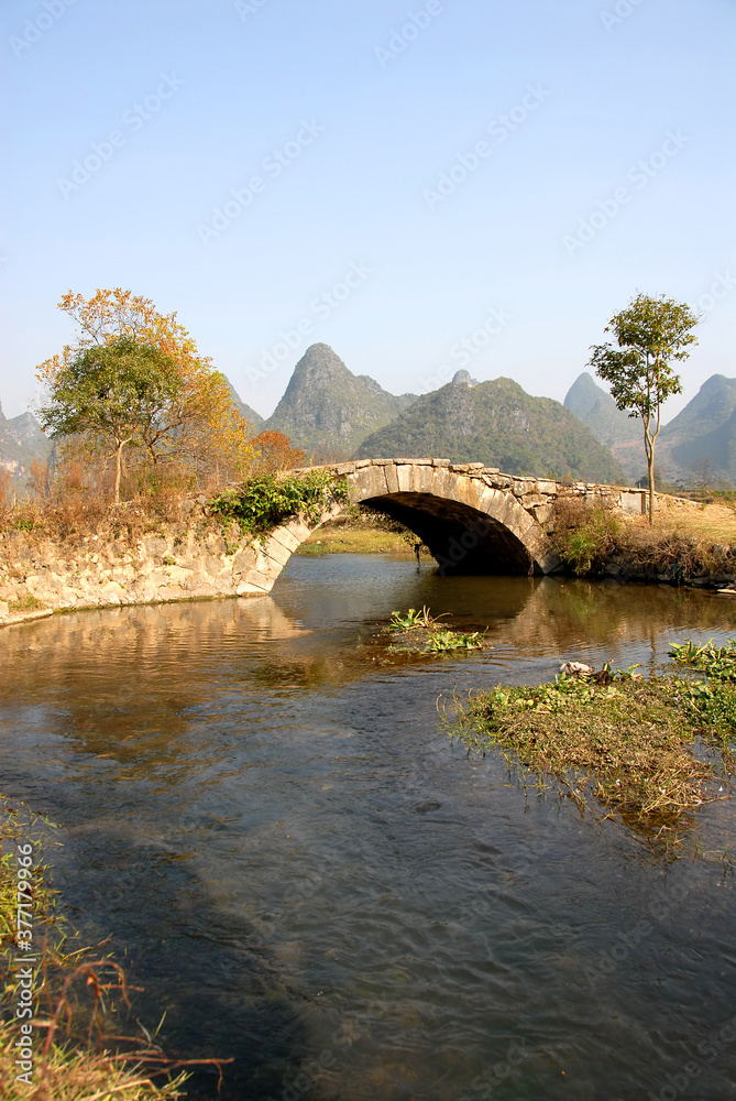 Fototapeta premium Scenery along the Yulong River near Yangshuo, Guilin in Guangxi Province, China. An ancient stone bridge near Yangshuo. The old bridge crosses a stream connecting farmland near to the Yulong River.
