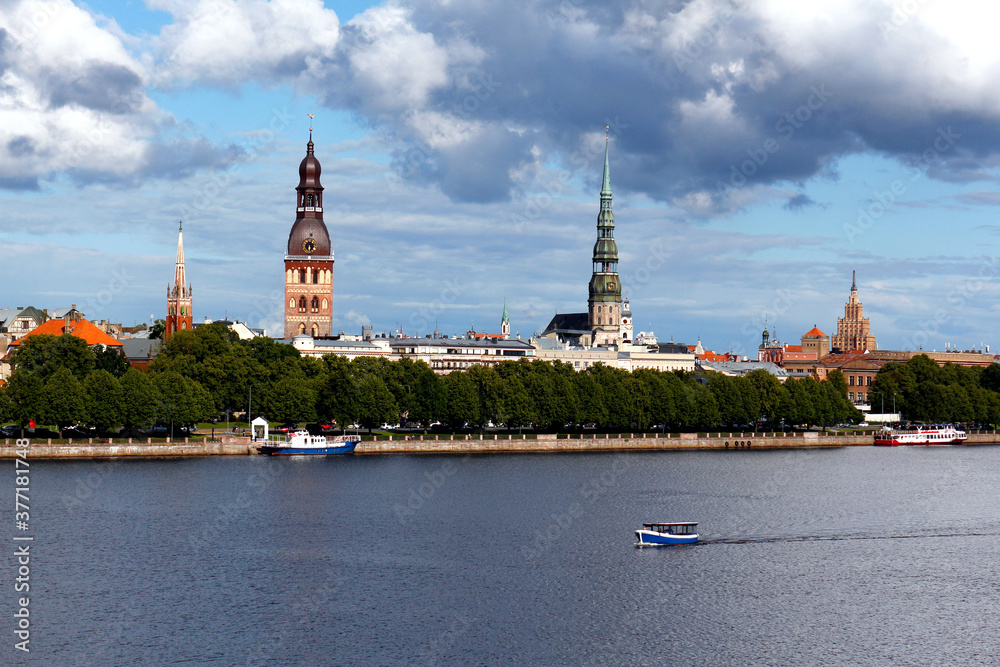 Obraz premium Beautiful panoramic view of the old town of Riga, Latvia. Amazing cityscape with clouds and a boat floating on the river.