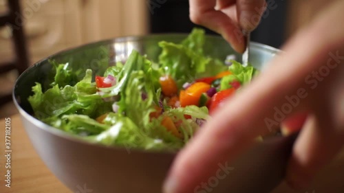 A female chef mixes raw vegetables and salad greens in a salad plate