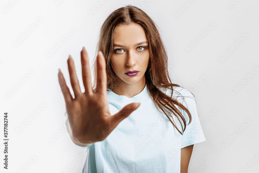 Stop. Enough. Young beautiful girl stretches out her hand to the camera to stop the effect. Woman with fashion makeup with purple lips on an isolated gray background. Bad events, despair and threat. Stop. Enough. Young beautiful girl stretches out her hand to the camera to stop the effect. Woman with fashion makeup with purple lips on an isolated gray background. Bad events, despair and threat.