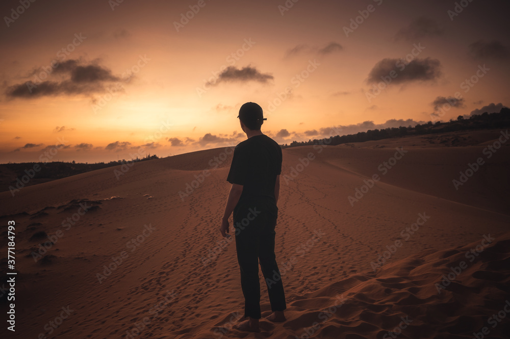 Traveler man with cap standing on dune at sunset