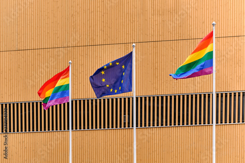 Obraz na płótnie The Pride flags and European Union flag on white flagpoles against the wooden wall. w salonie