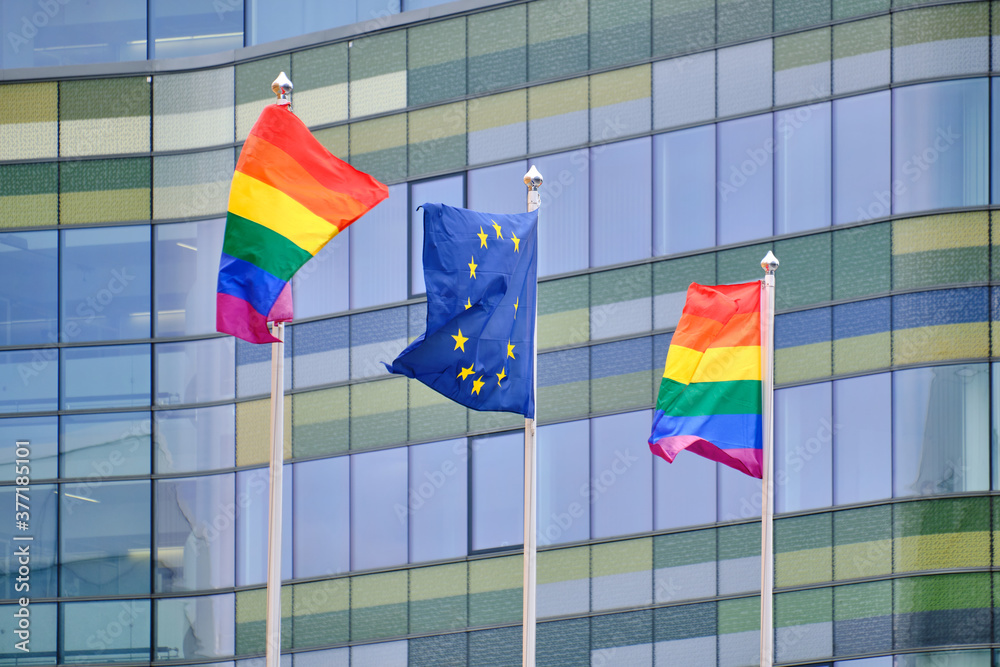 The Pride flags and European Union flag on white flagpoles against the modern building.