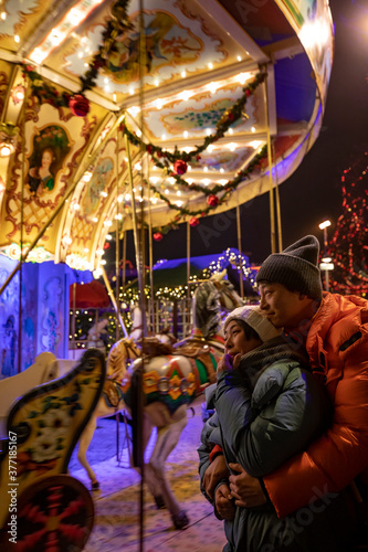 Happy couple in warm clothes on the carousel background in the colorful Christmas market photo