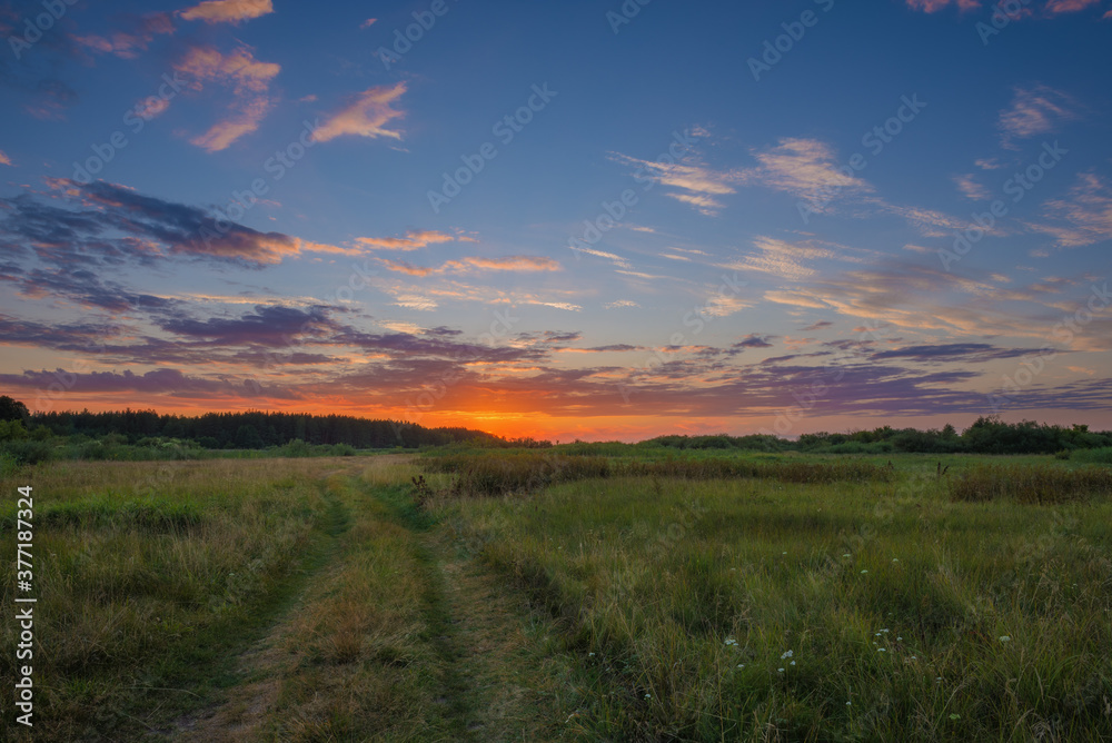 Landscape with country road in meadow against beautiful sunset