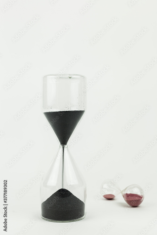 Vertical shot of two sand clocks made with glass on a white background. Time running and tempus fugit concept with copy space. Vertical shot of two sand clocks made with glass on a white background. Time running and tempus fugit concept with copy space.