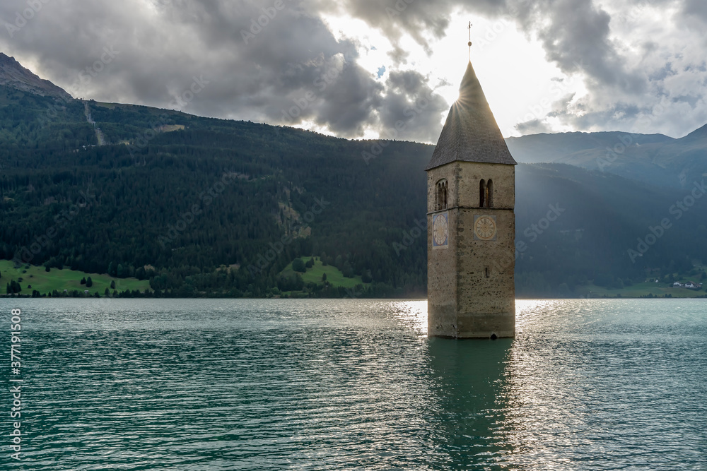 The sun peeps out from the top of the old bell tower of Curon Venosta, submerged in Lake Resia, South Tyrol, Italy
