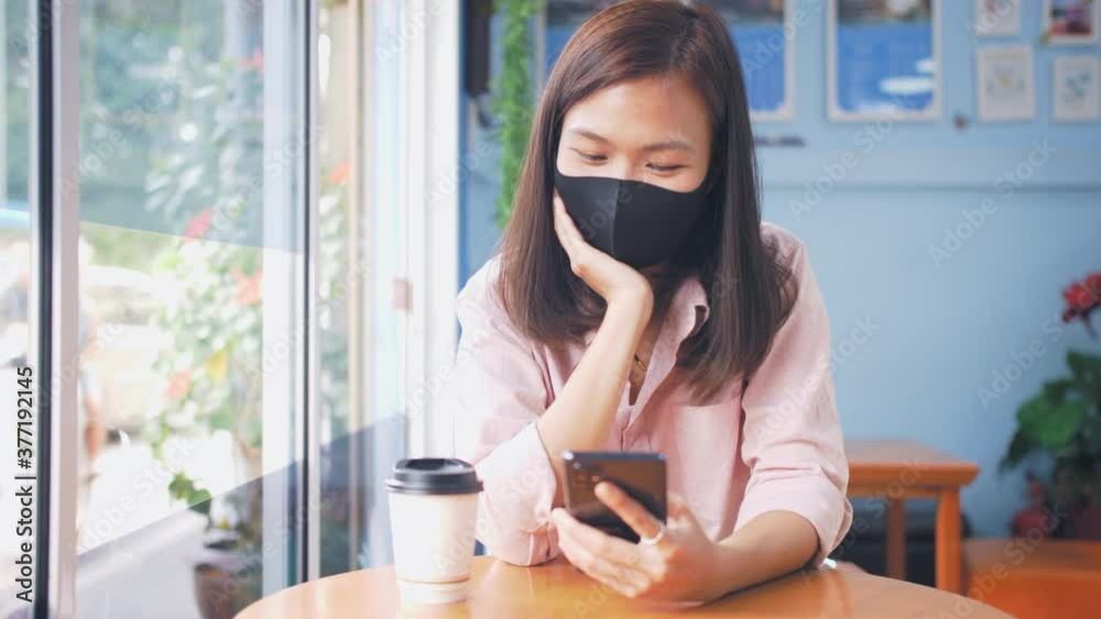 Beautiful woman asian wearing a mask is looking smart phone and smiling during the virus crisis , Concept Covid-19, New normal Beautiful woman asian wearing a mask is looking smart phone and smiling during the virus crisis , Concept Covid-19, New normal
