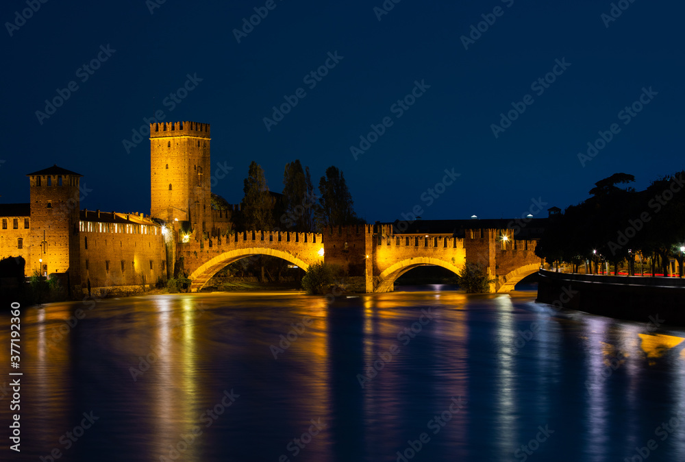 Illuminated bridge at night in Verona over the Adige River. Night landscape of Castelvechio Bridge. The sky and the lights on the bridge are reflected in the water