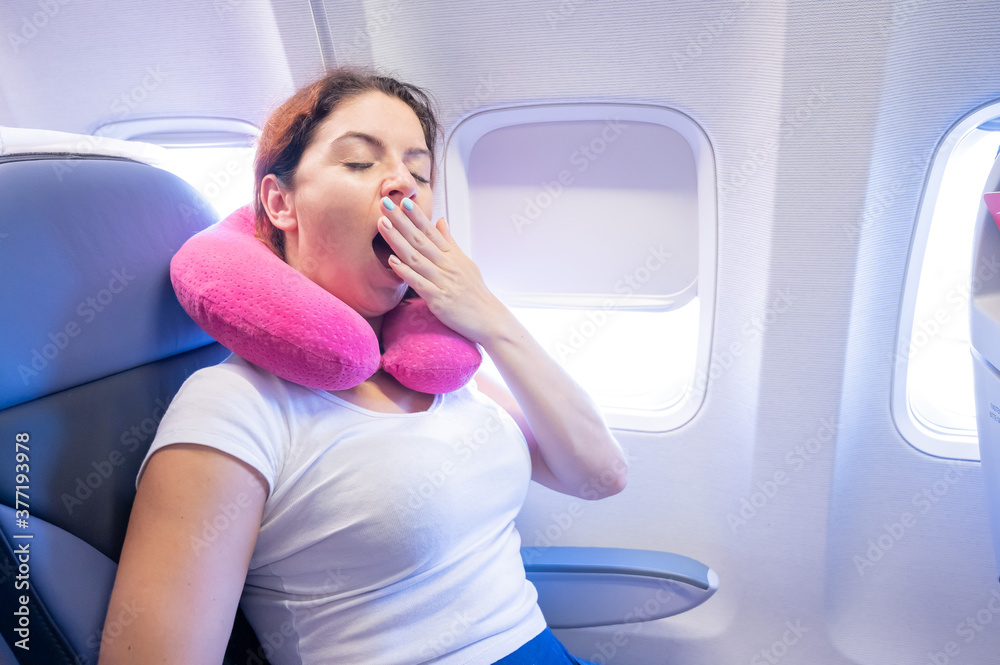 Woman yawns while sitting on the plane by the window. Woman yawns while sitting on the plane by the window.