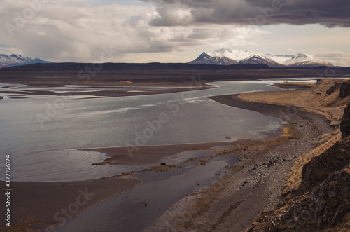 Sea landscape in Iceland. View of beach and mountain. The water is clear blue and low clouds dot the deep blue sky.