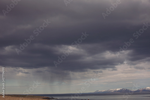 Sea landscape in Iceland. View of beach and mountain. The water is clear blue and low clouds dot the deep blue sky.