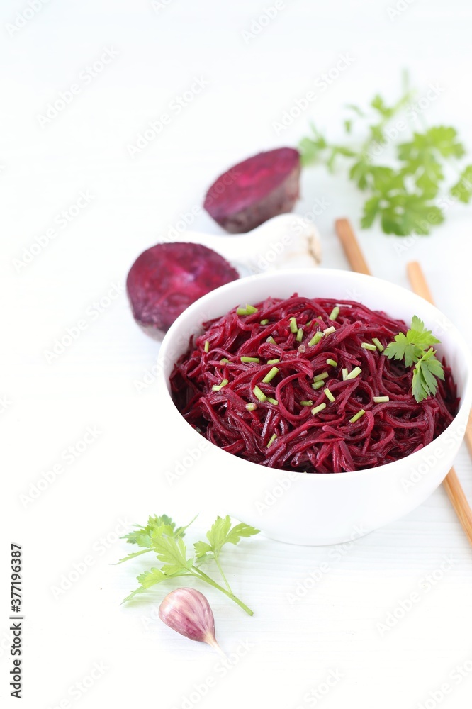 Korean beetroot salad with garlic and parsley in a bowl with wooden sticks on a white background Korean beetroot salad with garlic and parsley in a bowl with wooden sticks on a white background