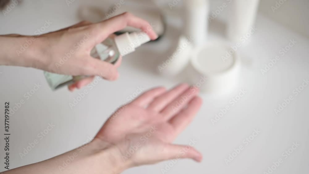 Woman at the table with cosmetics splash antiseptic lotion on her hands. Alcohol solution in a transparent dosing bottle to protect against bacteria in home. Cleansing cosmetic beauty product Woman at the table with cosmetics splash antiseptic lotion on her hands. Alcohol solution in a transparent dosing bottle to protect against bacteria in home. Cleansing cosmetic beauty product