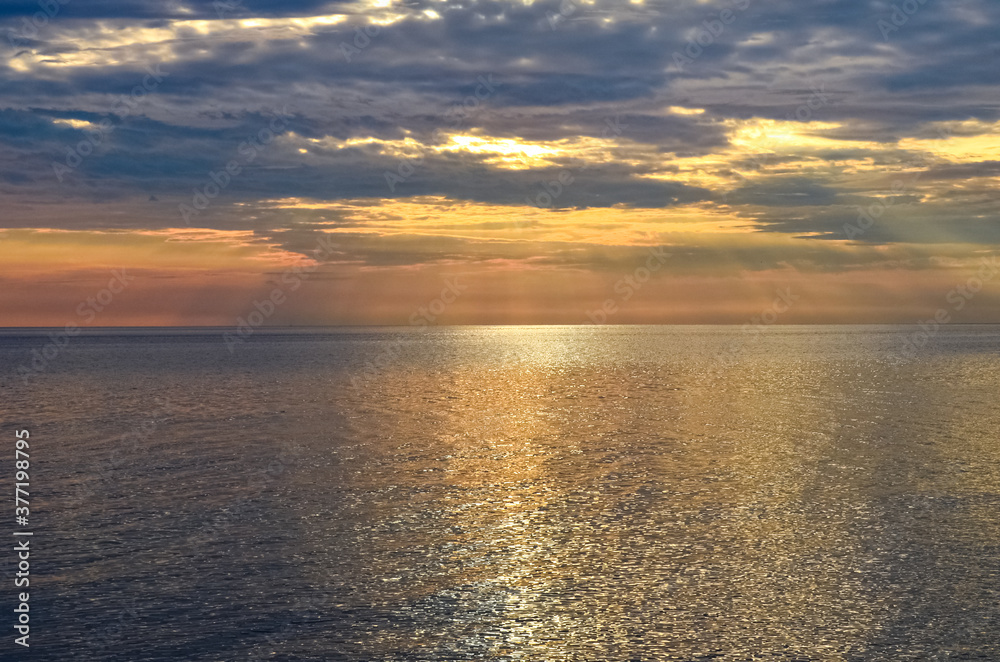 Golden sunset with dark clouds on the sea waters. Light reflection. 