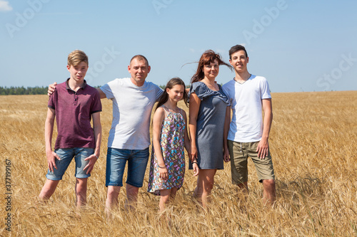 Three preteen children with their parents, large family portrait on wheat field, people standing in line, looking at camera