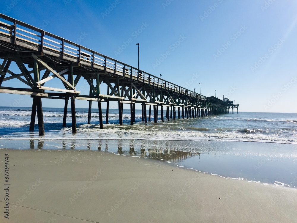 Cherry Grove Pier jutting out into the ocean in North Myrtle Beach, with blue sky, sea waves and sands. No matter what time of year, the Myrtle beach can be a relaxing and refreshing place to visit. 