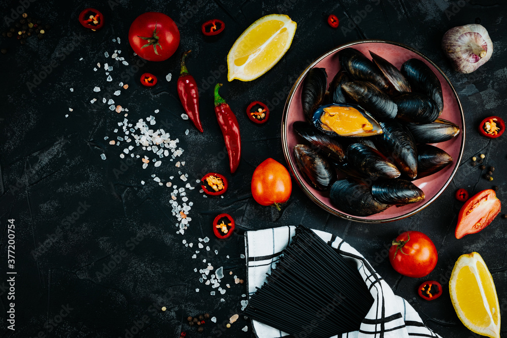 Ingredients for cooking pasta with seafood on a black background. Black spaghetti on a wooden background, top view, free space for text