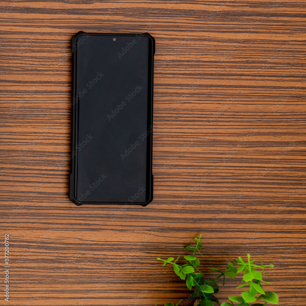 A black mobile phone on a striped brown working table with a calculator and a green plant A black mobile phone on a striped brown working table with a calculator and a green plant