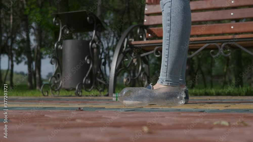 Plastic bottle in the park. The woman picks up an empty plastic bottle and throws it in the trash. Plastic bottle in the park. The woman picks up an empty plastic bottle and throws it in the trash.