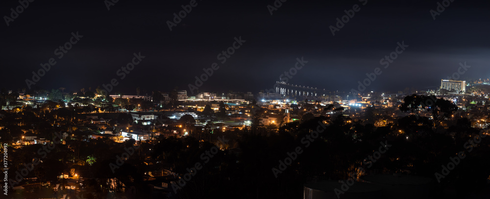Panoramic view of the coastal city of Ventura nestled against the Pacific Ocean at night with town lamps shining bright with a fog haze hovering overhead.