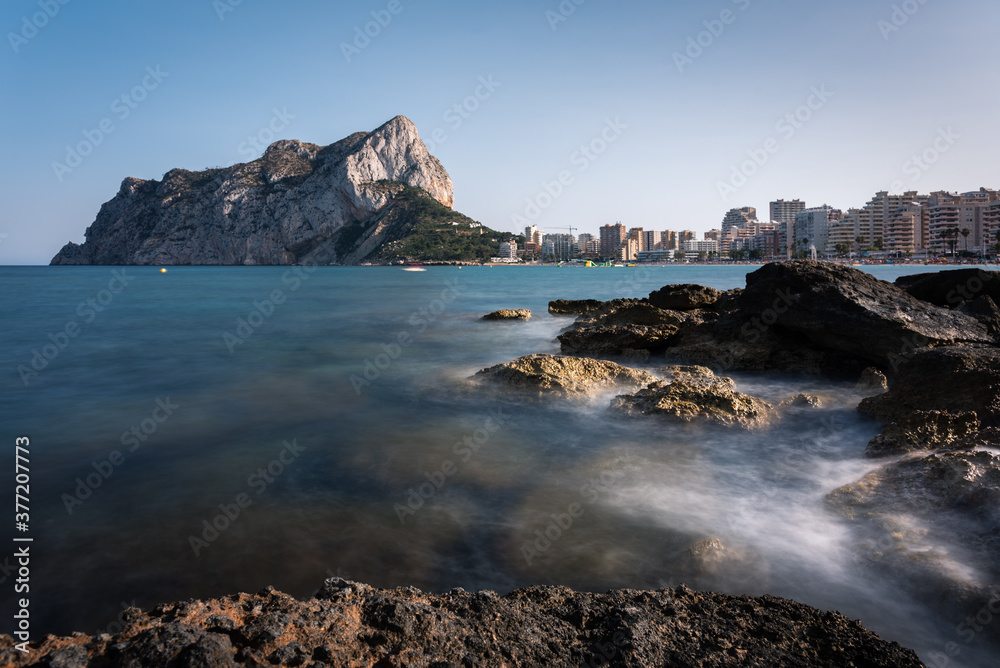 View from the rocks of the coastline with the urban beach of Calpe and the crag in the background, Alicante, Spain