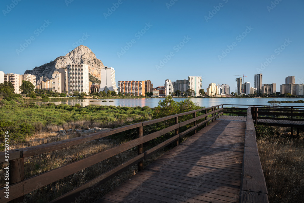 Fototapeta premium Footbridge in the salt lake of Calpe with the city skyline in the background, Alicante, Spain