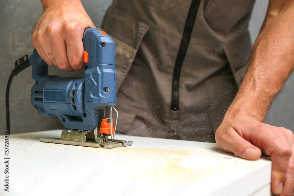 the hands of the builder are sawing with an electric jigsaw