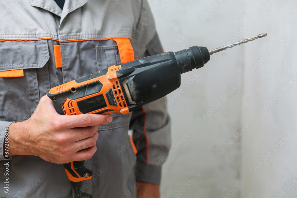 hand of the builder holds an hammer drill on background of gray wall with copy space
