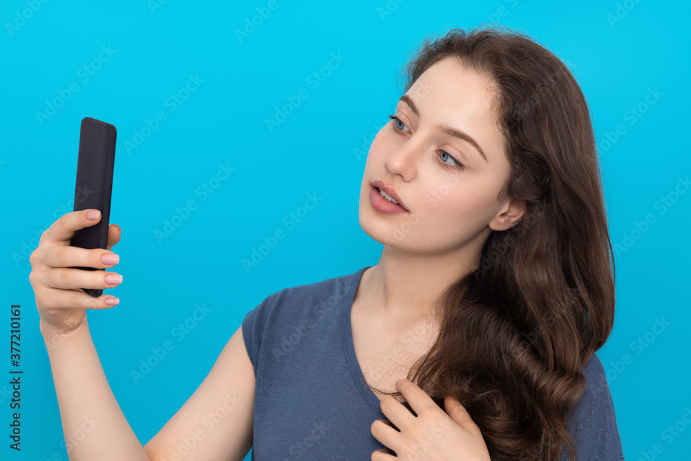 Young woman takes a selfie on blue background. Young woman takes a selfie on blue background.