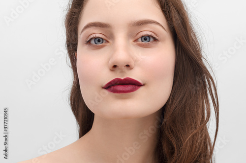 Woman with burgundy lipstick on her lips. Blue eyes, long hair and clear skin.