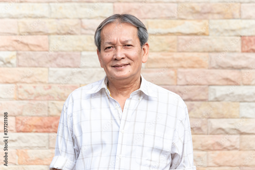 Portrait of smiling asian senior man standing in front of brick wall background with self confident manner. Closeup face of elder smile with gray hair. Portrait of smiling asian senior man standing in front of brick wall background with self confident manner. Closeup face of elder smile with gray hair.