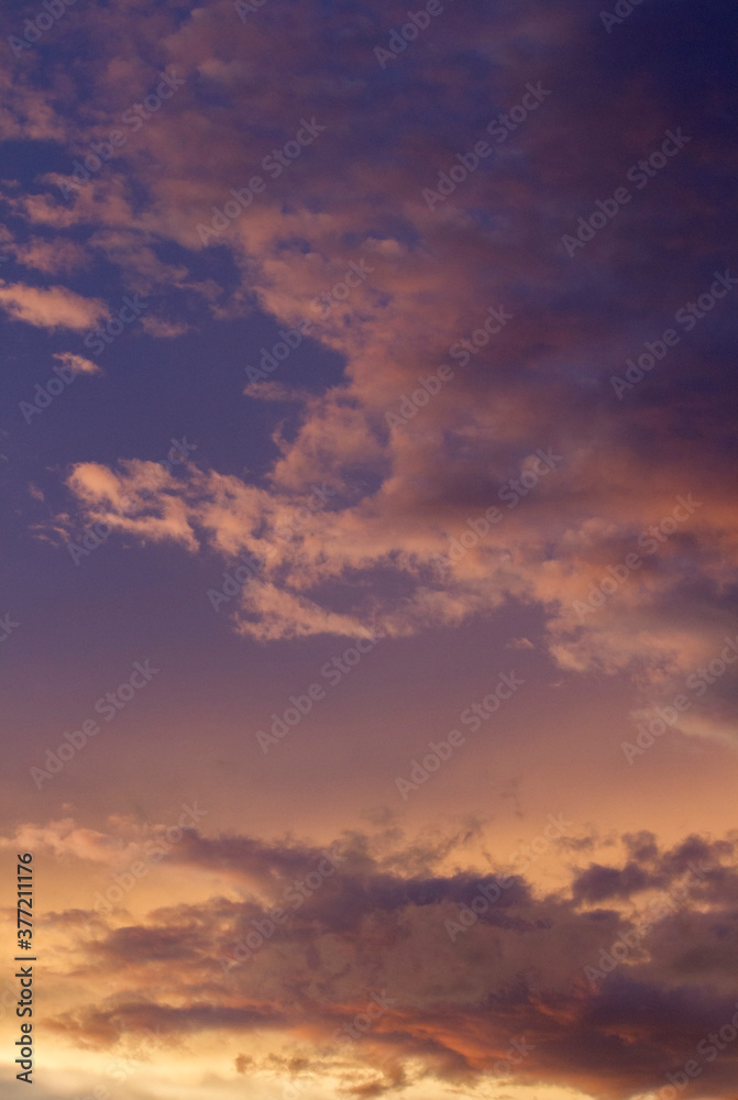 Vertical photo. Magical sunset. Cloudscape. View of the dramatic sky and clouds during twilight with beautiful dusk colors, purple, orange and magenta.