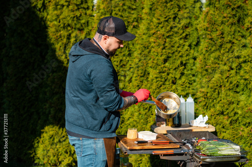 The cook mixes food in a saucepan. Concept of the correct cooking of meat. The chef prepares, fries a beef steak outdoors. Chef pours sauce on meat.