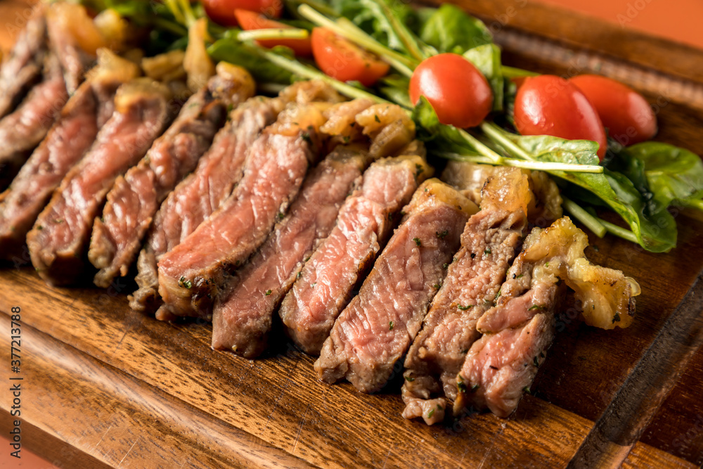 Beef steak on a wooden background. Sliced grilled meat barbecue steak Strip loin with knife and fork carving set on wooden Cutting board.Sliced freshly cooked steak with blood.