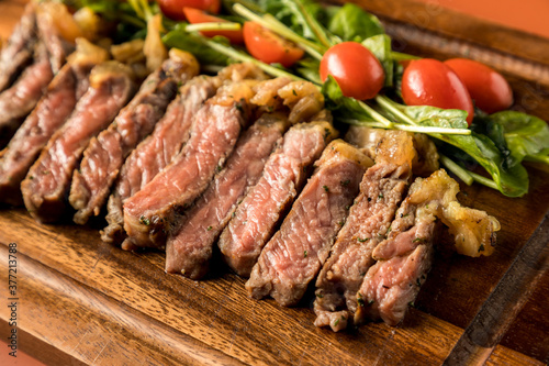 Beef steak on a wooden background. Sliced grilled meat barbecue steak Strip loin with knife and fork carving set on wooden Cutting board.Sliced freshly cooked steak with blood.