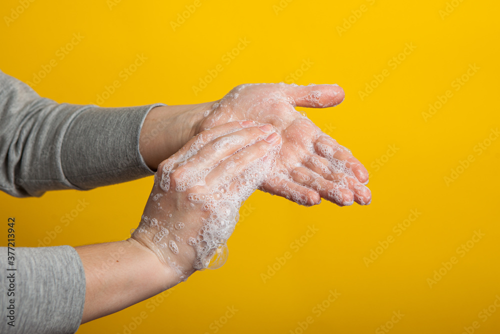 Fototapeta premium Instruction to carefully wash your hands and nails on a yellow background. Women's hands in a soap solution on a bright background