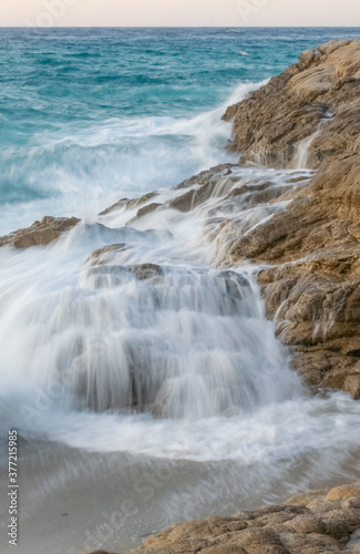 Vertical long exposure image of waves breaking against the rocks. Water flowing from the stones at the sand beaches of Ikaria, Island in the Aegean Sea, Greece