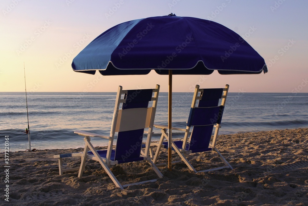 Lounge chairs under an umbrella on the beach at sunrise.