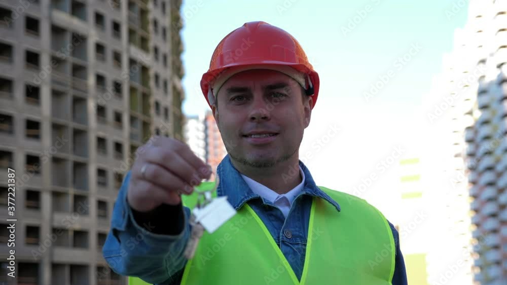 Worker engineer in yellow protective helmet show key at construction site. Outdoors Worker engineer in yellow protective helmet show key at construction site. Outdoors
