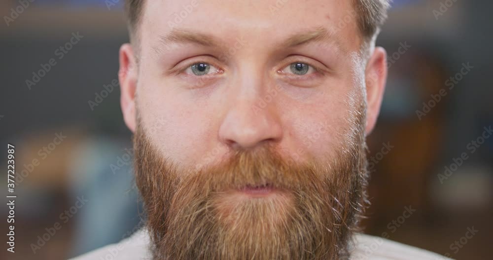 Closeup of smiling face of young bearded man, while barber arranges his hair.