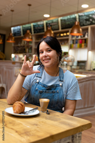 Young woman drinking coffee  making the sign of I love you