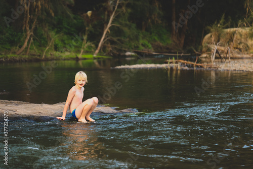 Boy sitting on rock looking at camera while swimming in natural swimming hole in central New South Wales, Australia