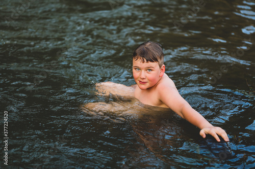 Boy swimming in river at dusk with big smile. Moody image with rich tones