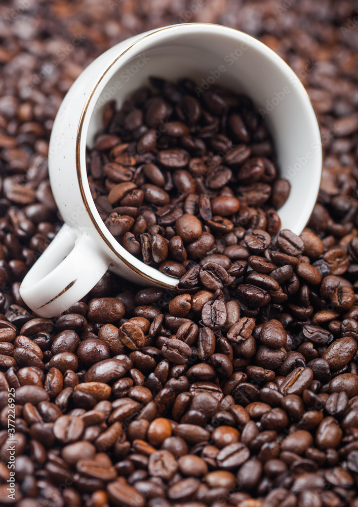 White ceramic cup with coffee beans inside fresh aroma roasted coffee beans background. White ceramic cup with coffee beans inside fresh aroma roasted coffee beans background.